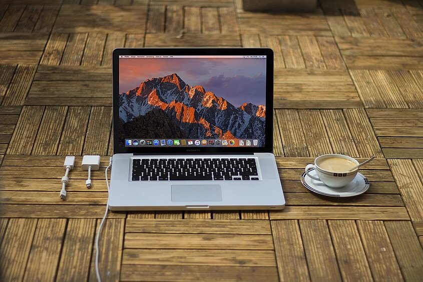 Laptop auf Tisch stehend mit Ladekabel und Kaffeetasse
