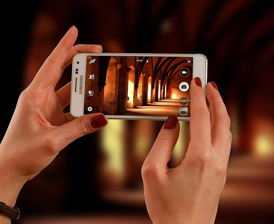 Zwei Hände halten ein Smartphone durch das gerade eine Sehenswürdigkeit fotorgrafiert wird